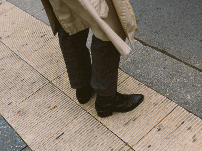 Person standing on a street in a tan coat and black boots