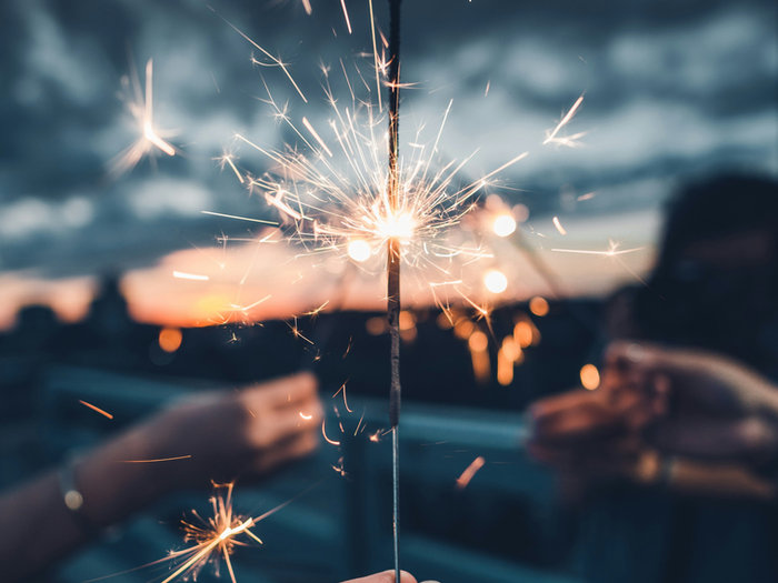 Hands holding a lit sparkler against a cloudy evening sky