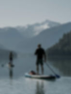 Two people paddleboarding on a lake near snowy mountains.