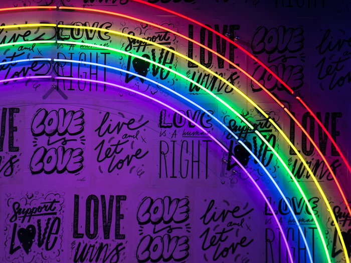 Neon rainbow sign on a wall of hand-painted slogans