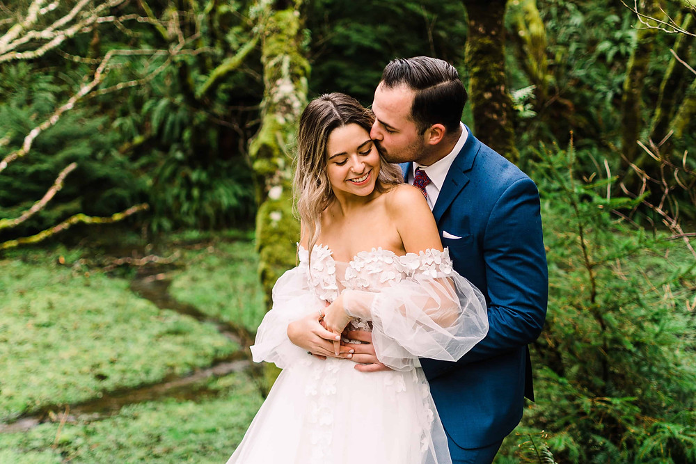 A couple embraces on their wedding day in a lush green forest in the Pacific Northwest