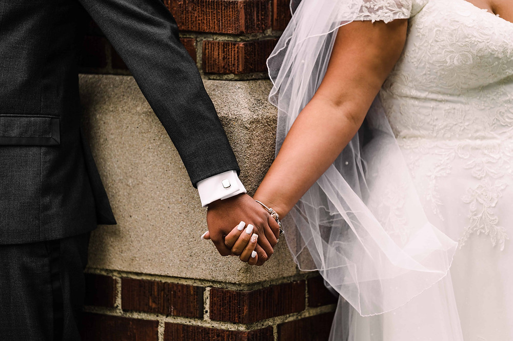 Two hands grasp each other at the corner of a building on a couple's wedding day; the bride and groom are having a "first touch" instead of a first look.