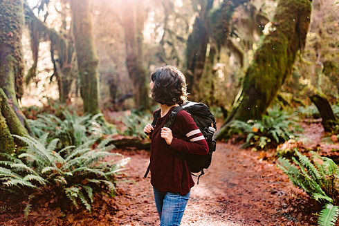 A woman in a maroon sweater looks around the Hoh Rainforest in Olympic National Park, holding her photography gear on her back.