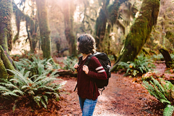 A woman in a maroon sweater looks around the Hoh Rainforest in Olympic National Park, holding her photography gear on her back.