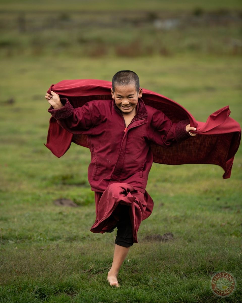 Smiling young monk running happily and freely in the green valleys of Bhutan symbolizing peace and happiness