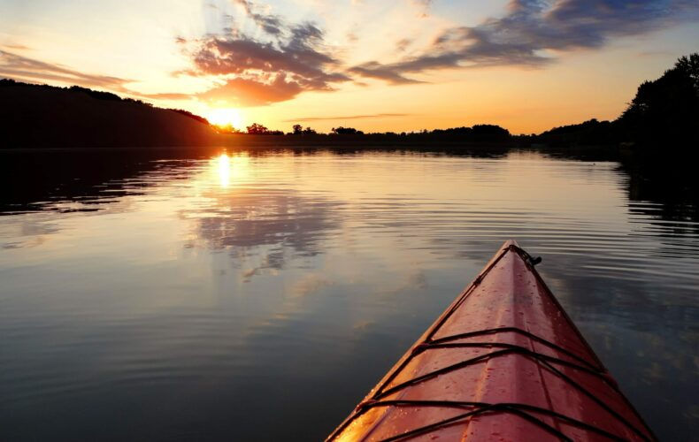 Paddlers view of bow of kayak against a sunset background with long fluffy clouds in the sky.