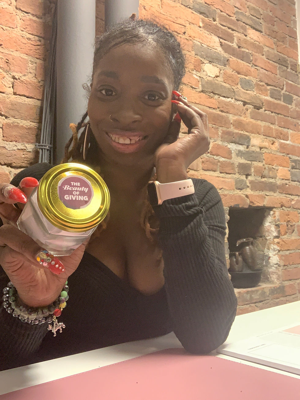 Coach Melony Hill smiling, wearng a black shirt and holding a glass jar. The lid of the glass jar says " the beauty of giving"