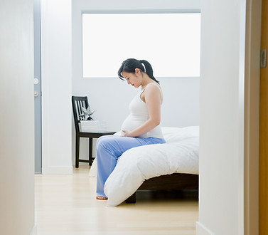 A pregnant woman sitting on a bed looking at her bump