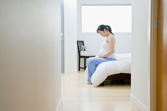 Schwangere Frau sitzt auf dem Bett