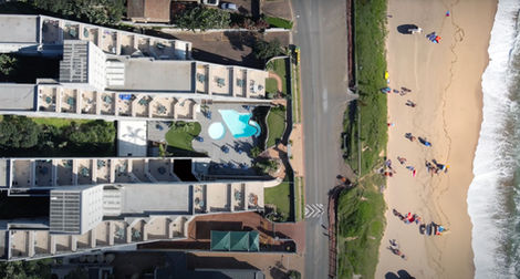 Aerial view of Umdloti apartments beside sandy beachfront with people walking