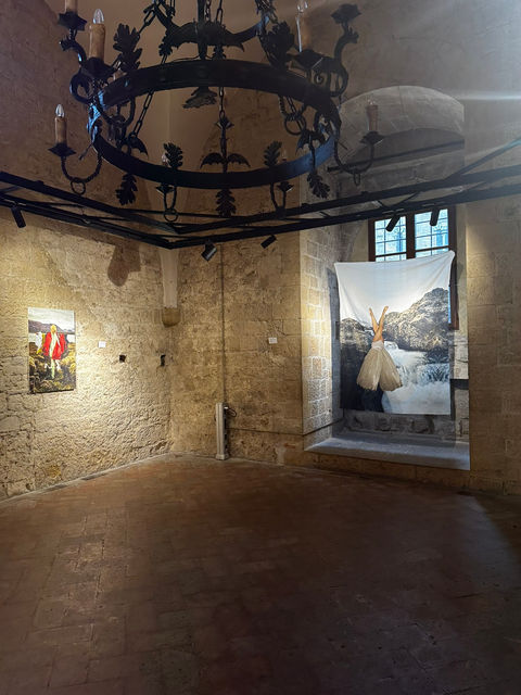exhibition room with brick walls and iron chandelier in medieval style with artworks by Telma Har on the wall.