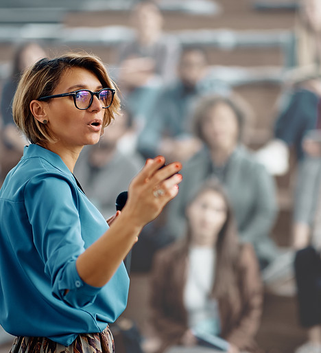 Eine Frau Mitte 40 hält einen Vortrag. Im Hintergrund sind die Zuhörer zu sehen.