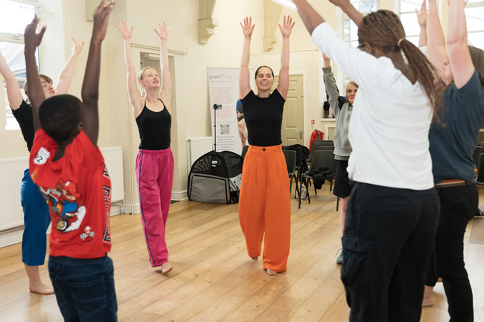 people in a circle with their hands stretched up in the air, some are smiling, as part of a movement workshop