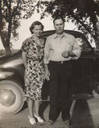 black and white image of a couple standing in front of a 1950s car