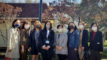 마스크 착용한 여성 9명 단체 사진, 건물과 나무 배경, 야외 활동