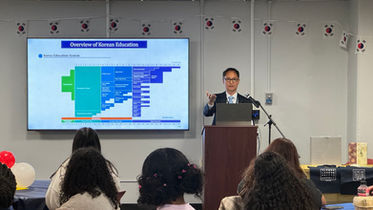 한 남자가 발표, 칠판에는 표, 교육원 활동, 청중은 발표를 듣습니다.