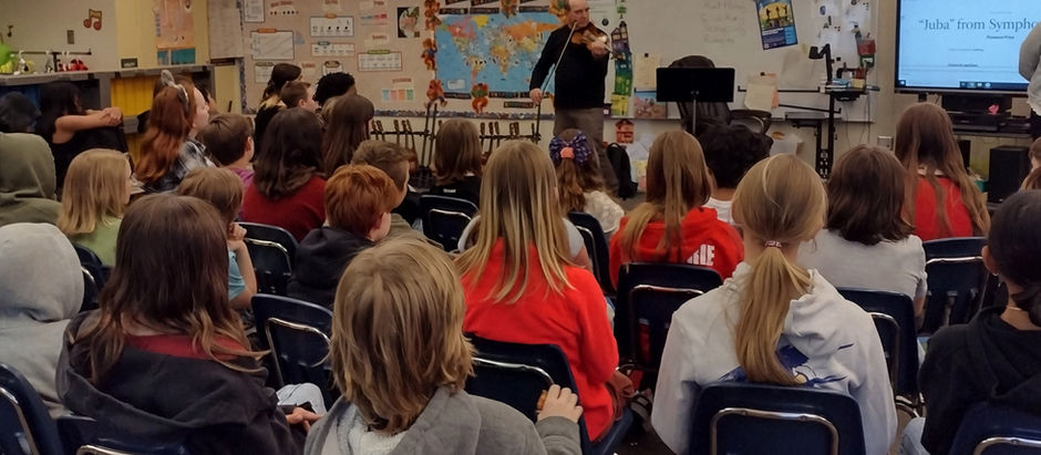 Children stand and smile in a colorful classroom as a man plays a violin. Musical notes and educational posters are on the walls.