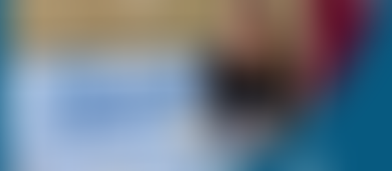 Katie Lee and Stefan Keel stand smiling beside a "Spark" banner indoors. The banner has a blue and yellow star logo. Text below the Logo reads "Support. Partner. Advocate. Reach. Kindle. Helping teachers One Spark at a time.