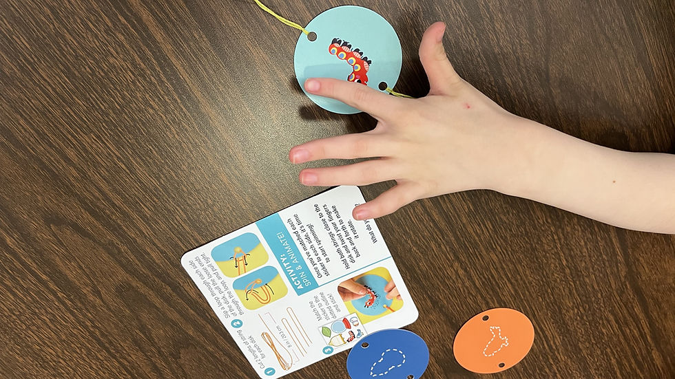 A child's hand spins a blue disc with a caterpillar on a wooden table. Instruction card visible, alongside blue and orange discs.