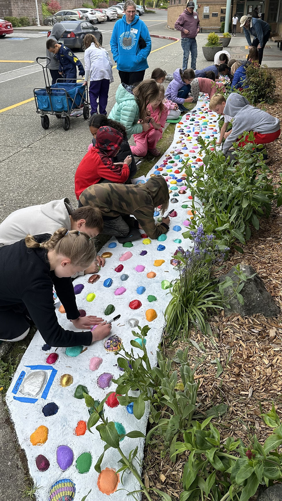 Children paint colorful stones on a white pathway outdoors.