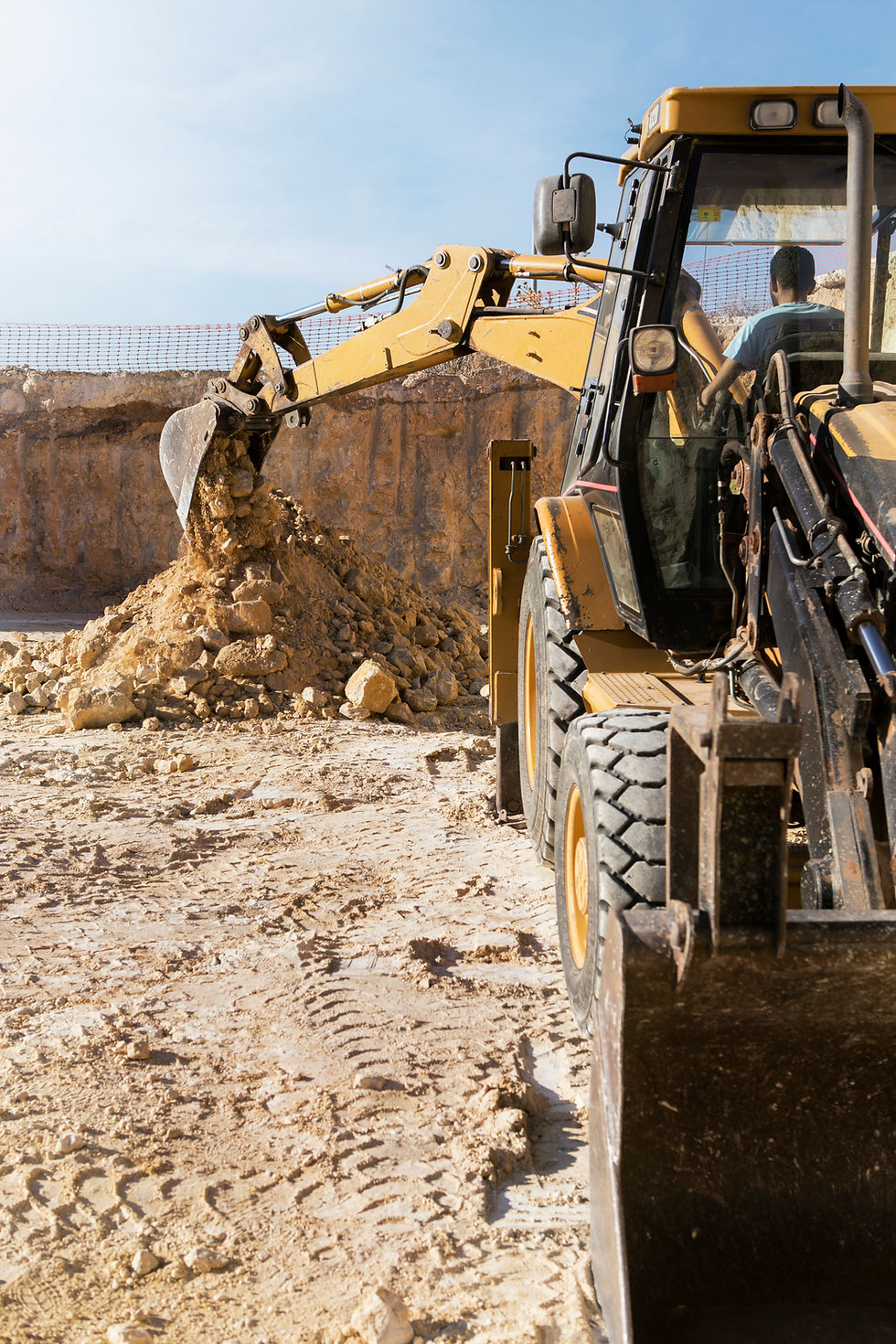A yellow excavator scoops soil, construction worker, working on Excavation Services