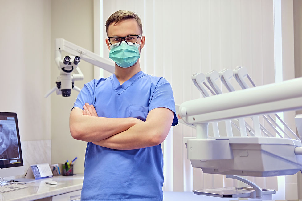 A male dentist in scrubs poses in a modern dental clinic setting