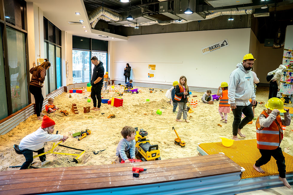 Children playing with construction toys in a large indoor sandbox.