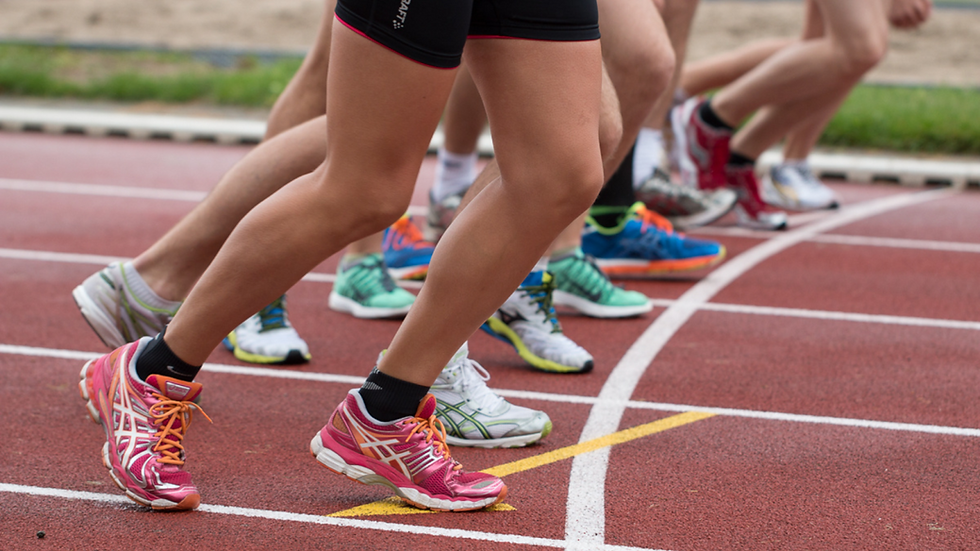 Runners' legs in colorful athletic shoes at starting line on track, demonstrating active calf muscles