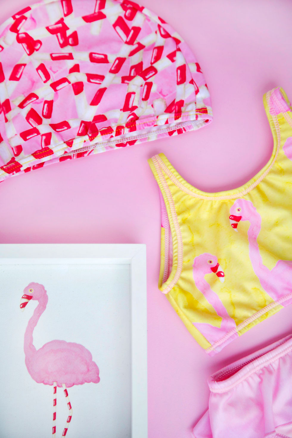 Thumbnail: vestido de baño bikini rosado amarillo ilustrado con flamingo de algodon de azucar rosado  con bolero rosado en el bikini y gorro de lycra color rosado ilustrado con pitillos rojos y blancos con cuadro de ilustracion de flamingo de algodon de azucar rosado y patas de pitillo blancas y rojas en fondo rosado