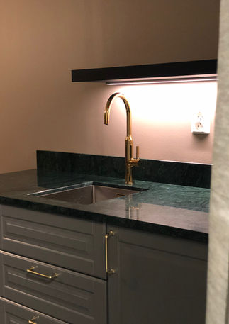 Guldvattenkran över diskho med mörkgrön bänkskiva och grå skåp.