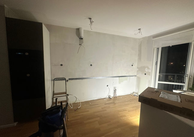 Rum under renovering med avskalade väggar, synliga kablar och trägolv.