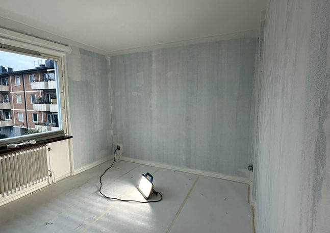 Renoveringsrum med ljusblåa väggar, vit golvskyddsduk och fönster mot stad.