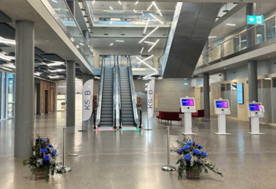 Patient Intake Flow im Kantonsspital Baden: Helles, grosszügiges Eingangsfoyer mit heyPatient Self-Check-in Terminals, KSB-Bannern und Rolltreppe, bereit für den strukturierten Patientenempfang.