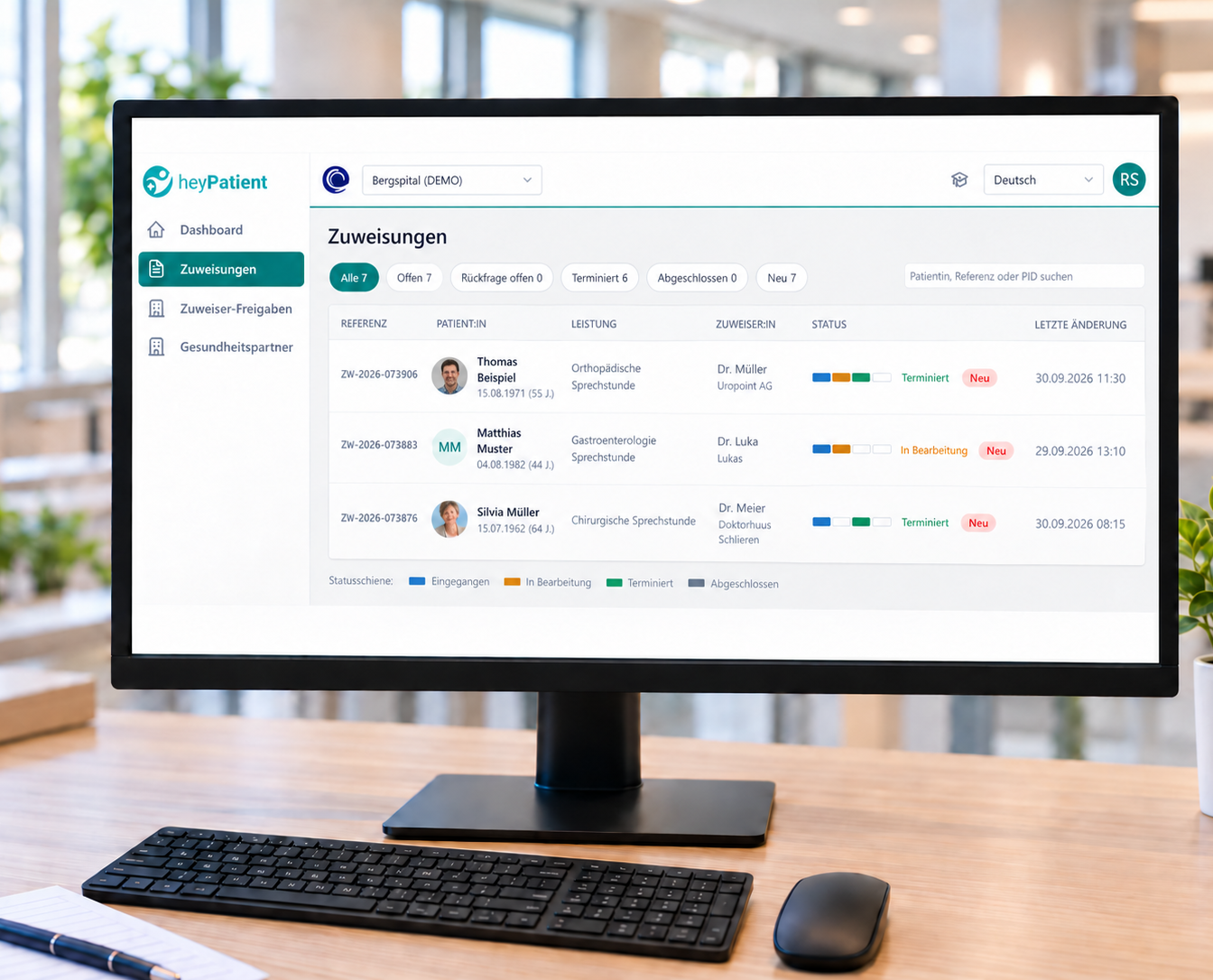 Monitor zeigt heyPatient mit Zuweisungen im Krankenhaus; auf dem Schreibtisch Tastatur und Maus, helles Büroambiente.