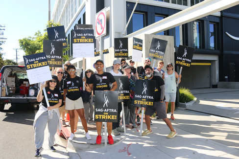 A group photo of fifteen people wearing "SAG-AFTRA STRONG" tshirts and holding SAG-AFTRA picket signs.