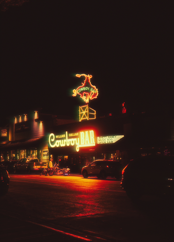 A cinematic nighttime photograph of a glowing cowboy bar sign captured in Jackson Hole Wyoming, showcasing western lifestyle and nightlife. This image highlights moody lighting, bold color tones, and storytelling through visual content, perfect for brands and businesses looking for high end social media content creation and western inspired photography.