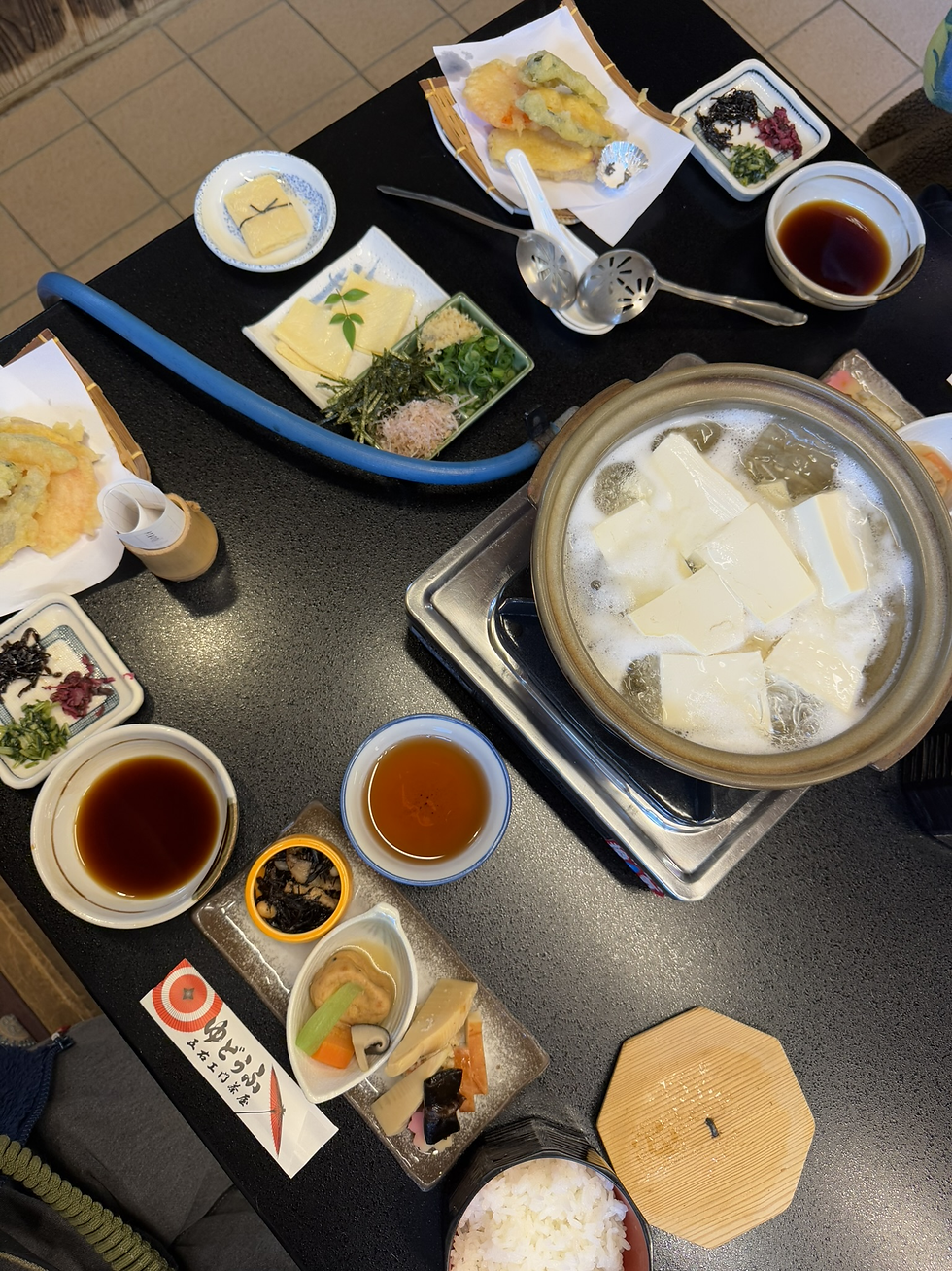 俯视日式餐桌:锅中煮着豆腐和高汤,周围有天妇罗、豆腐小菜、酱油碟、茶杯和白饭,氛围丰盛安静。