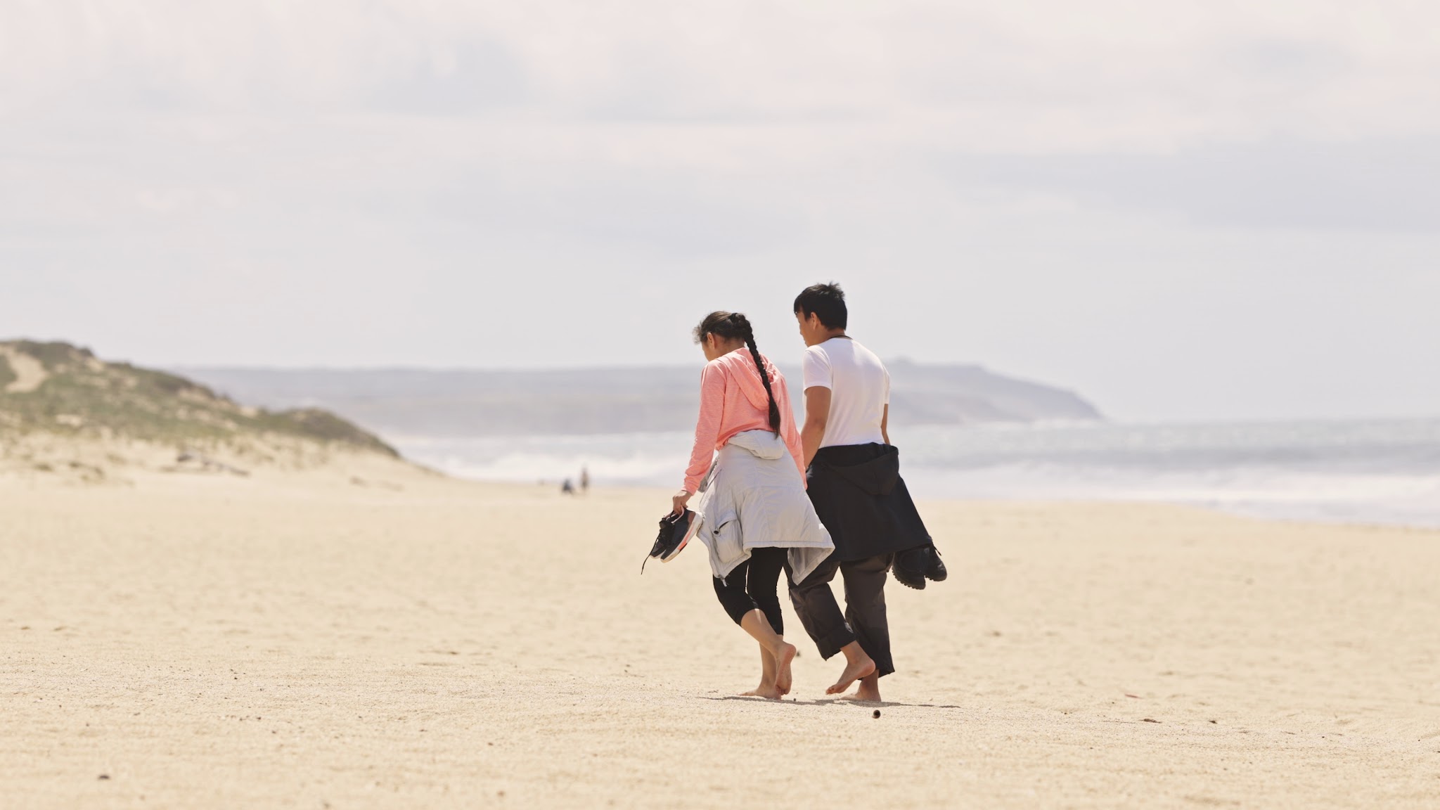 Couple walking along a beach beneath a cloudy sky