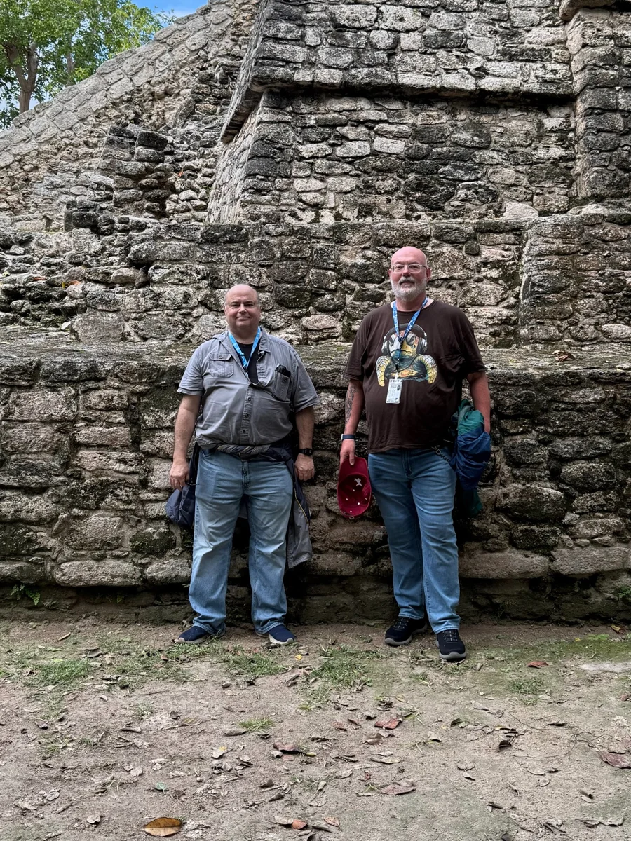 Two travelers standing beside the stone ruins at Chacchoben