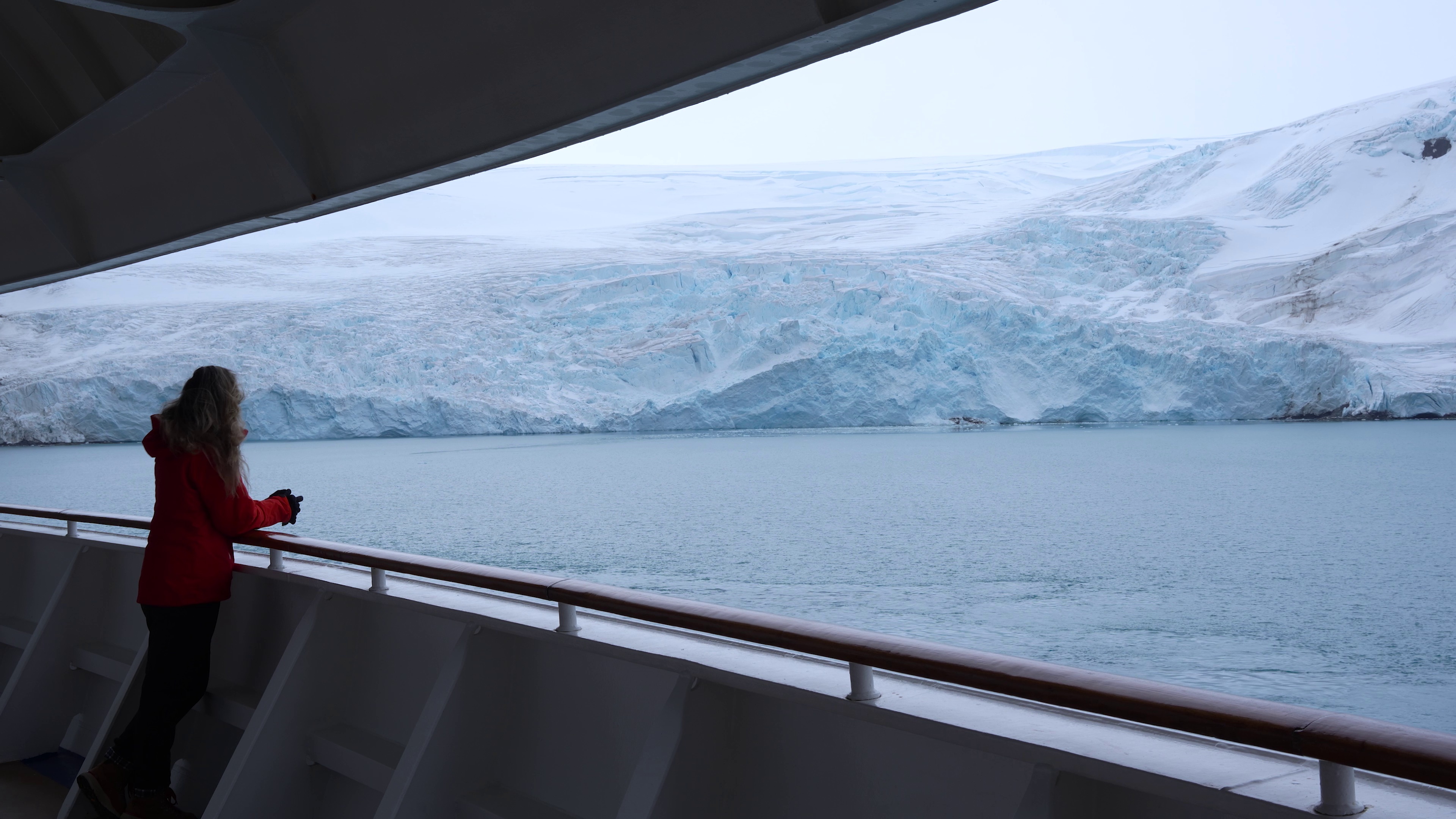 Solo cruise traveler enjoying a view of Antarctic mountains from a ship deck