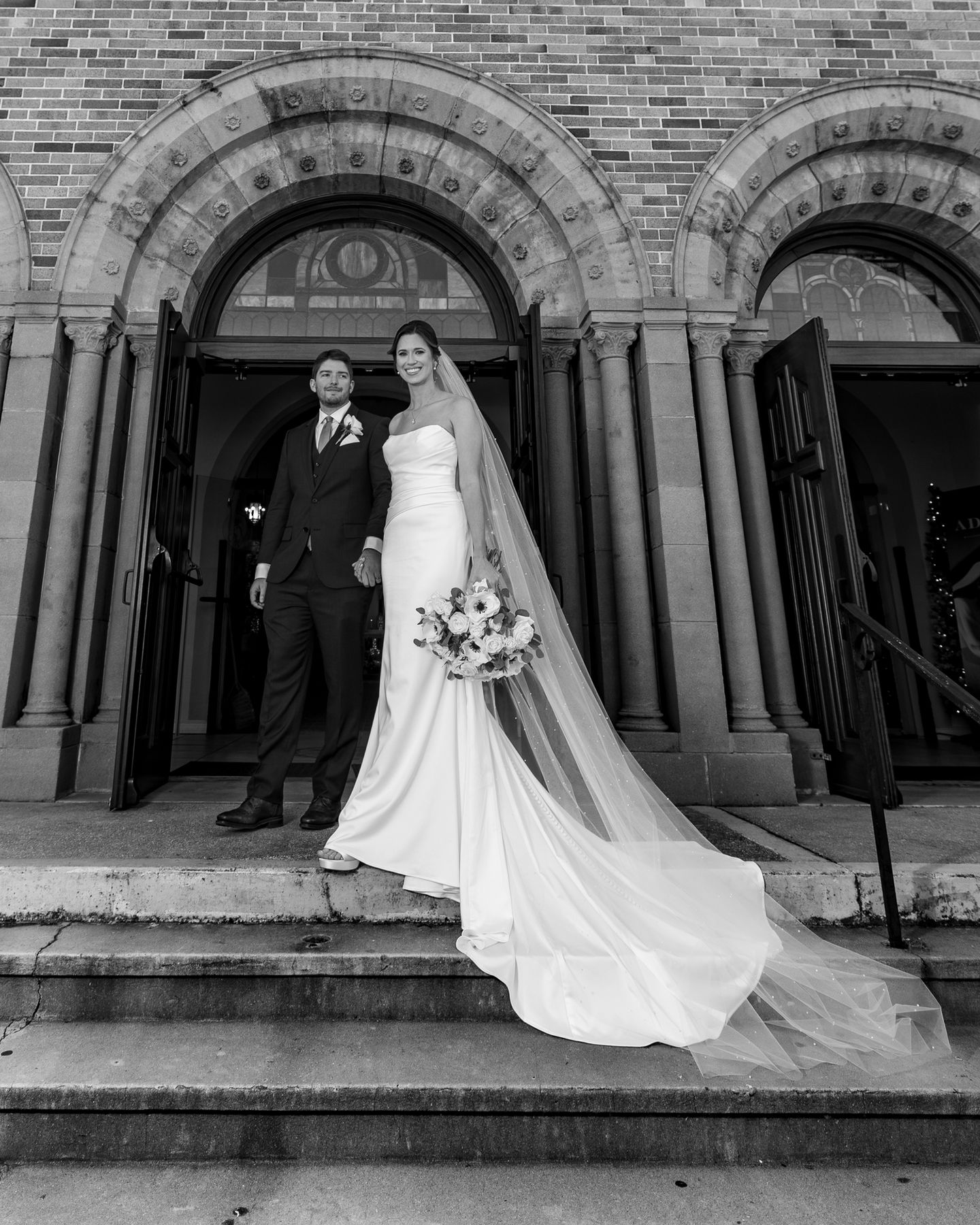 a black and white photo of a bride and groom in front of a church