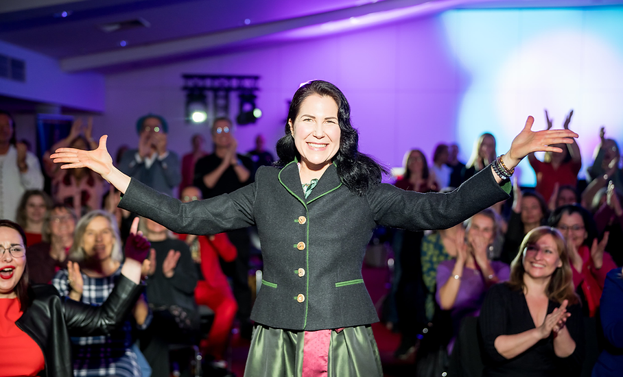 Sylvia als Rednerin auf einer Veranstaltung im Vordergrund. Umringt von vielen Menschen die Applaudieren