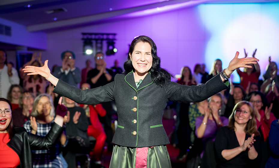 Sylvia als Rednerin auf einer Veranstaltung im Vordergrund. Umringt von vielen Menschen die Applaudieren