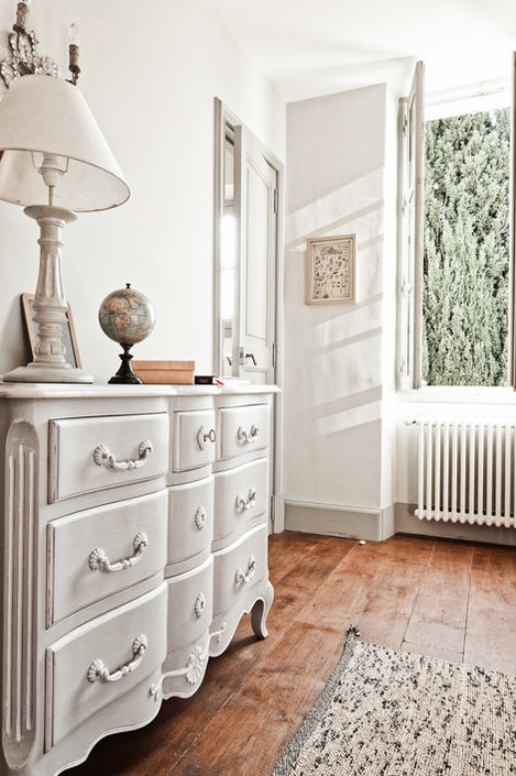 A well-lit children's bedroom featuring two single beds with floral-patterned bedding. The walls are decorated with framed butterfly art and a vintage anatomical poster. A bedside table with a lamp and a teddy bear adds a charming touch to the space