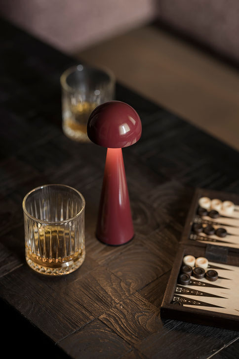 Lampe ZANZI QOOZII coloris Cerise allumée sur une table en bois, jeu de backgammon et verres de whisky