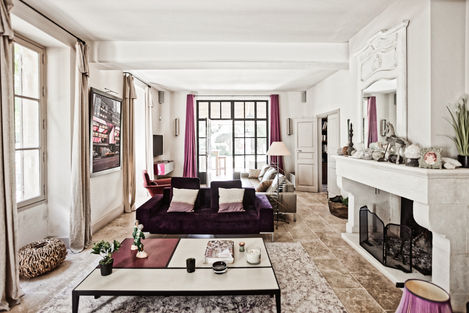 main living room of Mas de Campe, a luxurious rental property near Saint Rémy de Provence. The room is spacious and comfortable, featuring a large purple sofa, a modern coffee table, and an elegant fireplace. The natural light from the windows enhances the serene ambiance, making it a perfect place to relax
