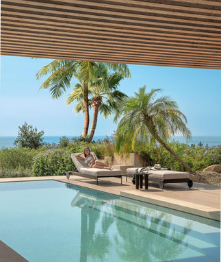 Bains de soleil FLOW Talenti installés au bord d’une piscine avec vue mer et palmiers