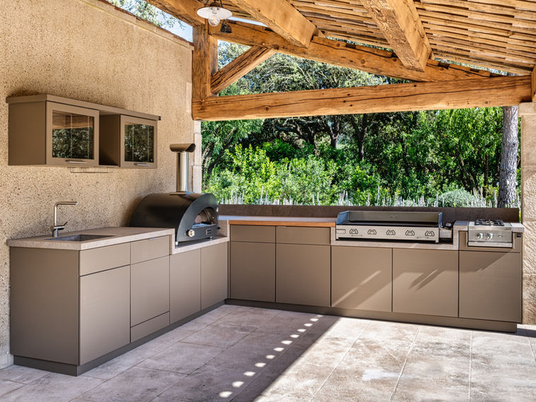 Cuisine extérieure sur-mesure sous pergola en bois, équipée d’un four à pizza, d’une plancha et d’un évier, alliant design élégant et matériaux résistants aux intempéries