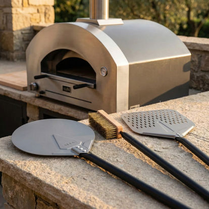 Accessoires du set de pelles ALFA Forni à côté d’un four à bois installé en cuisine extérieure
