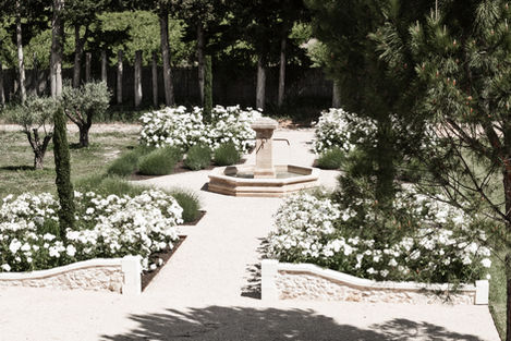 An overhead view of the garden pathways leading to the central fountain, flanked by neatly trimmed bushes and white flowers